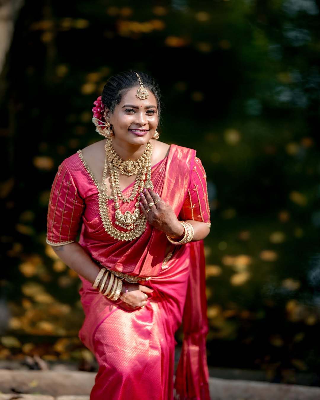 Woman in pink saree with traditional gold jewelry, smiling outdoors