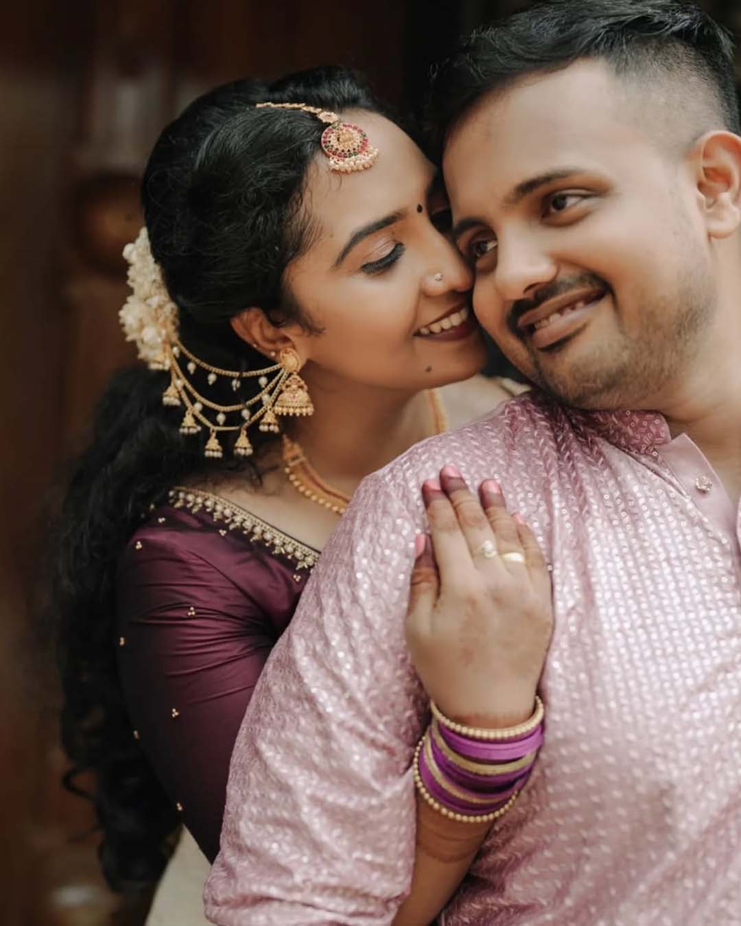 Happy couple in traditional wedding outfits sharing a close moment, bride wearing purple saree and gold jewelry
