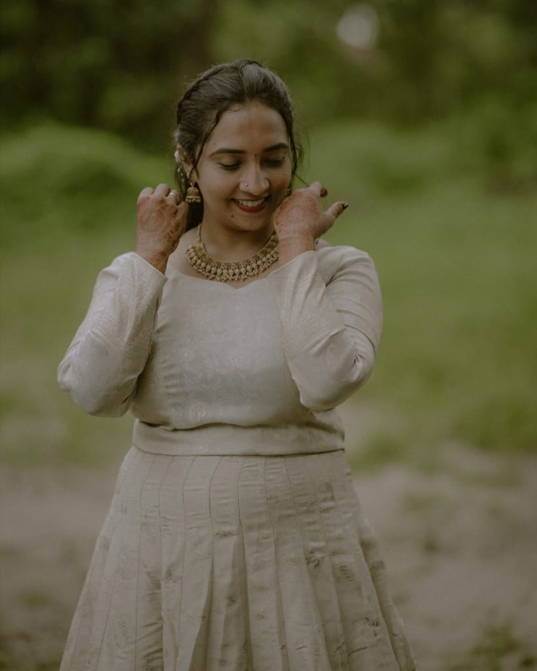 Smiling woman in white dress adjusting her earrings outdoors
